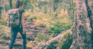 Woman wearing backpack and hiking clothes journeying uphill in a forested area